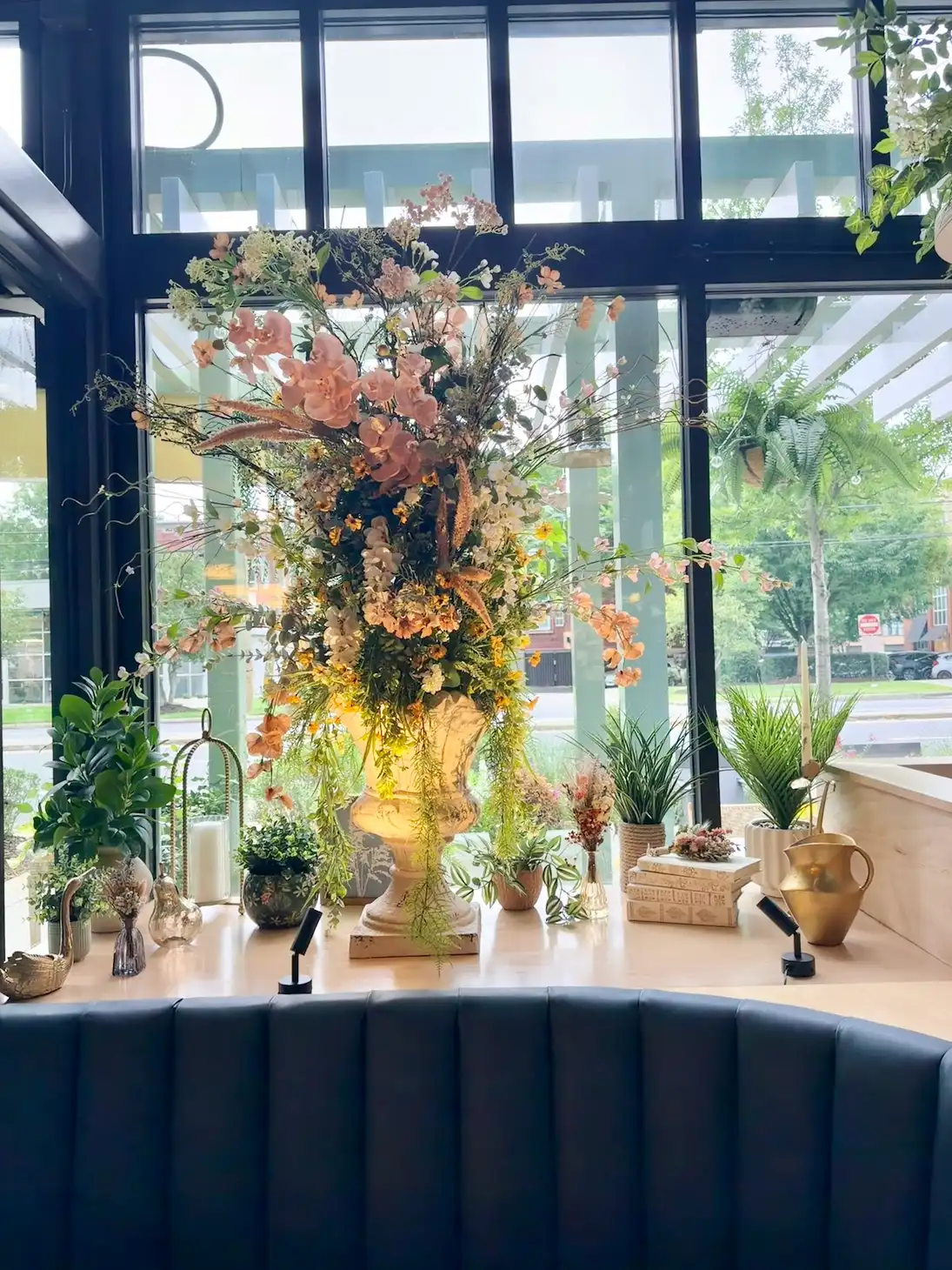 Large artificial floral arrangement in a pedestal urn behind a navy restaurant banquette