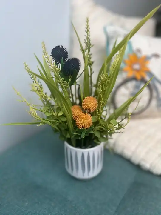 Blue thistle and yellow billy balls with grasses in a striped white planter